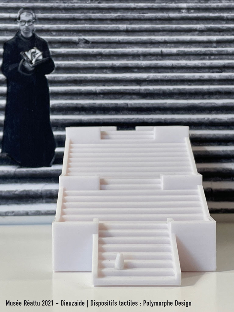 Au premier plan se trouve la maquette 3D de l'escalier de G&eacute;rone. En arri&egrave;re plan, la photographie de Dieuzaide remplit l'image de ses lignes horizontales. L'eccl&eacute;siastique apparait sur la gauche de l'image.